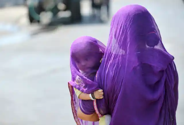 A woman carrying a child uses a part of her sari to shield themselves from sun on a hot summer day in Hyderabad. 