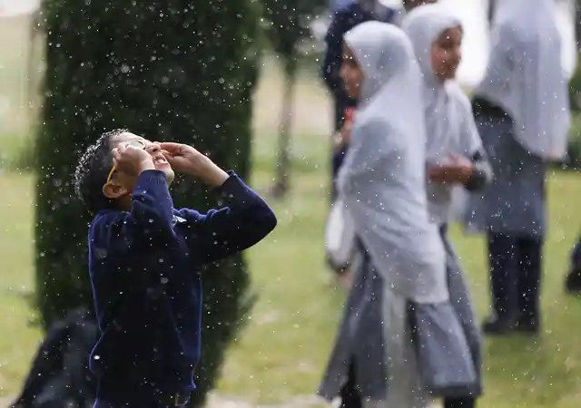 A Kashmiri school boy, on a picnic to Mughal garden, looks skywards as it rains in Srinagar, Tuesday, 30 April 2019. 
