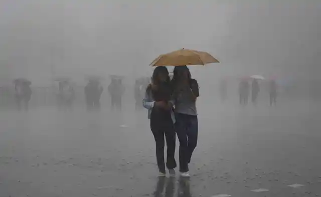 Pedestrians protect themselves with an umbrella during a downpour in the hill-station of Shimla on 24 June.
