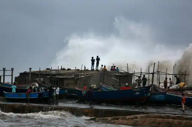 A wave crashes as people stand on boats on the Arabian Sea coast in Veraval, Gujarat, India, on Wednesday, 12 June.