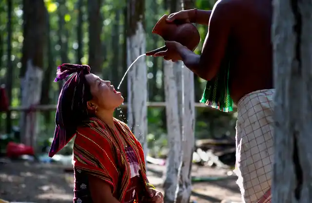 In this Monday, 10 June photo, an Indian Rabha tribal Hindu priest pours traditional rice beer to a Rabha girl to perform rituals during Baikho festival at Pantan village, west of Gauhati, India. Every year, the community in Assam celebrates the festival, to please a deity of wealth and ask for good rains and a good harvest.