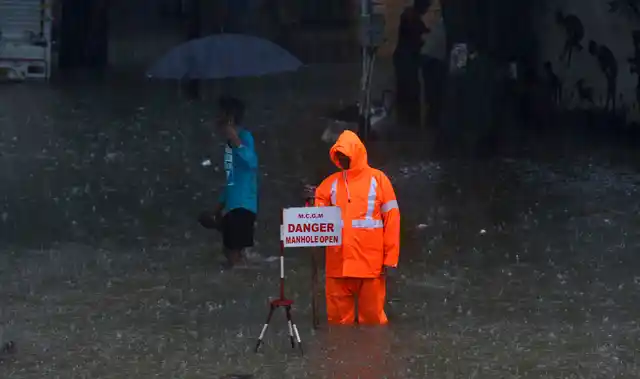 A municipal worker guards near an open manhole on a waterlogged street during monsoon rain in Mumbai.