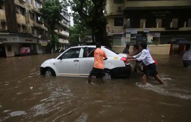 People push a car to a safer place from a waterlogged street during monsoon rains in Mumbai.