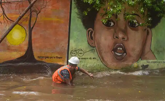 A Municipal worker cleans an open manhole on a waterlogged street following heavy monsoon rains, in Mumbai. 