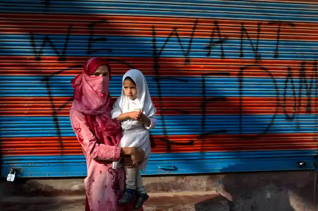 Jawahira Banoo carries her young daughter outside a closed shop with a spray-painted graffiti after a protest, 27 September 2019. 