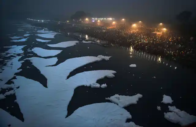 Devotees offers prayers as toxic foam floats on the surface of polluted Yamuna river during Chhath Puja celebrations, at Kalindi Kunj, in New Delhi.