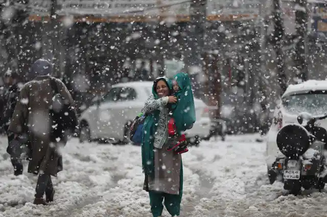 A Kashmiri woman covers her child with a shawl as they wait for transport in the snow in Srinagar. The region received its first snow on Wednesday, 6 November.