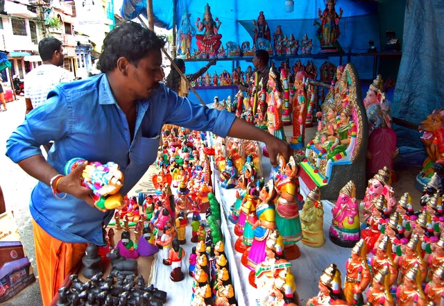 கொலு பொம்மைகளை விற்பனைக்காக அடுக்கி வைக்கும் தொழிலாளி