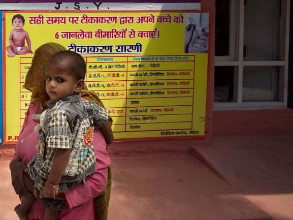 Patients walk past a wall with posters of polio awareness, and other child care precautions at the Primary Health Care Center building in Dhatrath, India. (Photographer: Prashanth Vishwanathan/Bloomberg)