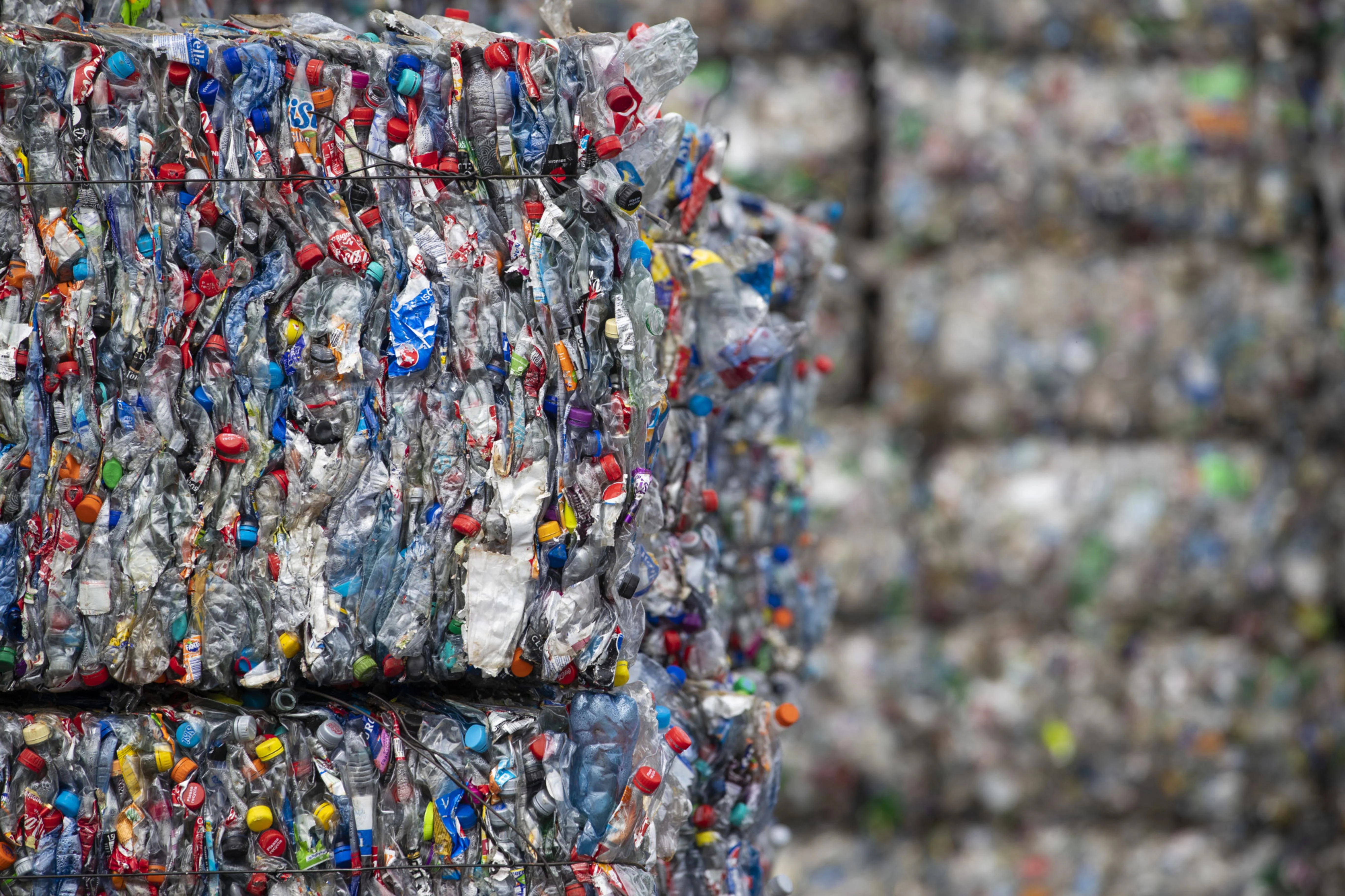 Bound bales of crushed plastic bottles and containers sit stacked ready to be recycled at a recycling centre. (Photographer: Jasper Juinen/Bloomberg)