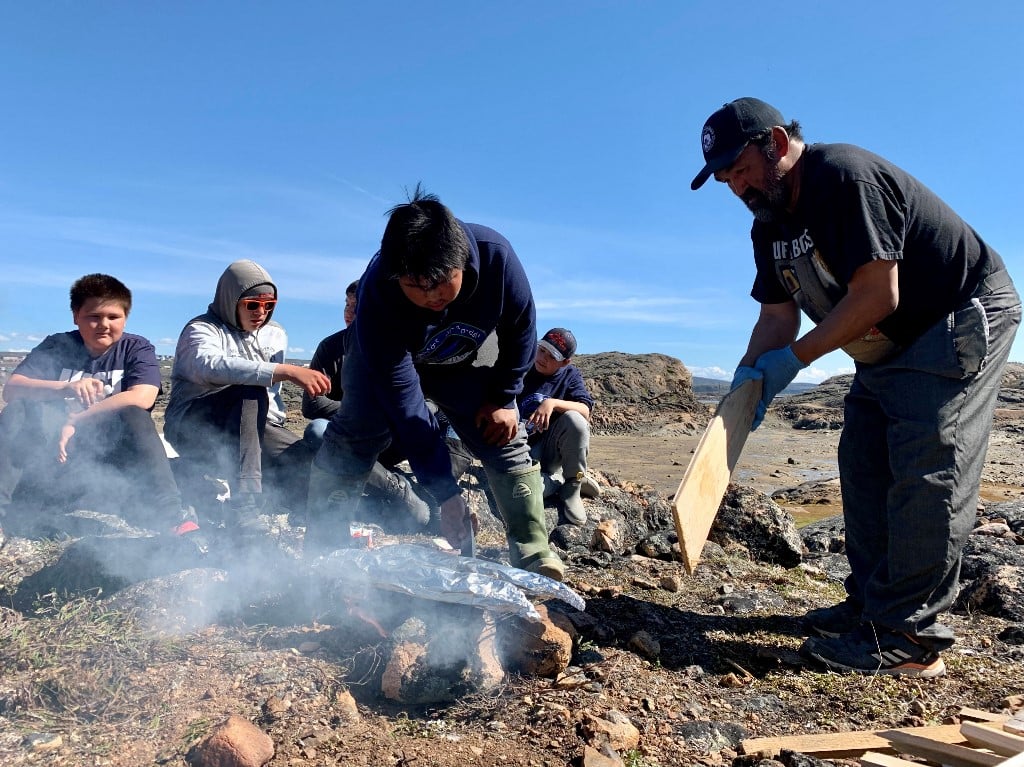 Inuit teens learn how to cook salmon over an open fire at a summer camp focused on mental health, in Iqaluit, Nunavut, Canada, on 27 July 2022. Filleting a fish, lighting a fire, or building an igloo in Canada's Arctic, a traditional hunter is reconnecting Inuit youth to their culture in order to save lives at risk from severe depression. (Photo by ANNE-SOPHIE THILL / AFP)