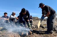 Inuit teens learn how to cook salmon over an open fire at a summer camp focused on mental health, in Iqaluit, Nunavut, Canada, on 27 July 2022. Filleting a fish, lighting a fire, or building an igloo in Canada's Arctic, a traditional hunter is reconnecting Inuit youth to their culture in order to save lives at risk from severe depression. (Photo by ANNE-SOPHIE THILL / AFP)