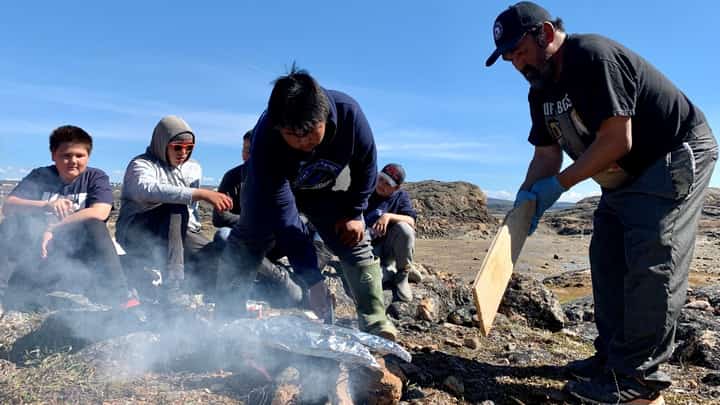 Inuit teens learn how to cook salmon over an open fire at a summer camp focused on mental health, in Iqaluit, Nunavut, Canada, on 27 July 2022. Filleting a fish, lighting a fire, or building an igloo in Canada's Arctic, a traditional hunter is reconnecting Inuit youth to their culture in order to save lives at risk from severe depression. (Photo by ANNE-SOPHIE THILL / AFP)