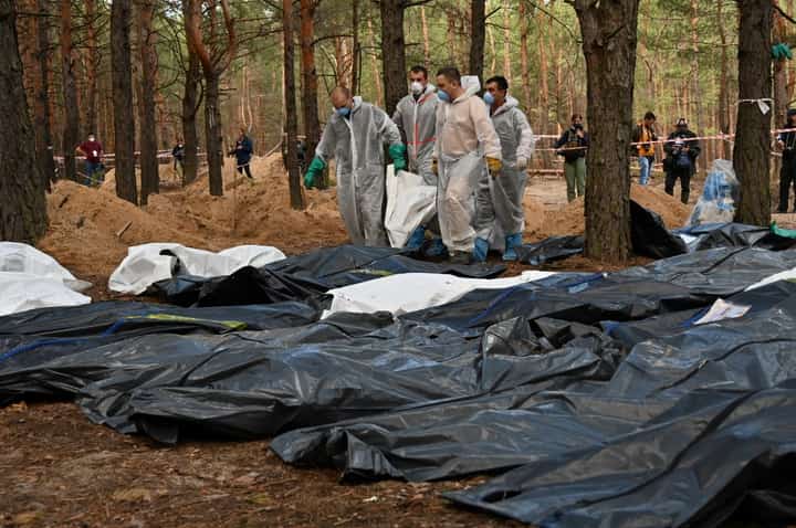 Forensics carry body bags in a forest near Izyum, eastern Ukraine, on 19 September 2022, where Ukrainian investigators have uncovered more than 440 graves after the city was recaptured from the Russians, bringing fresh claims of Russian atrocities. (Photo by SERGEY BOBOK / AFP)