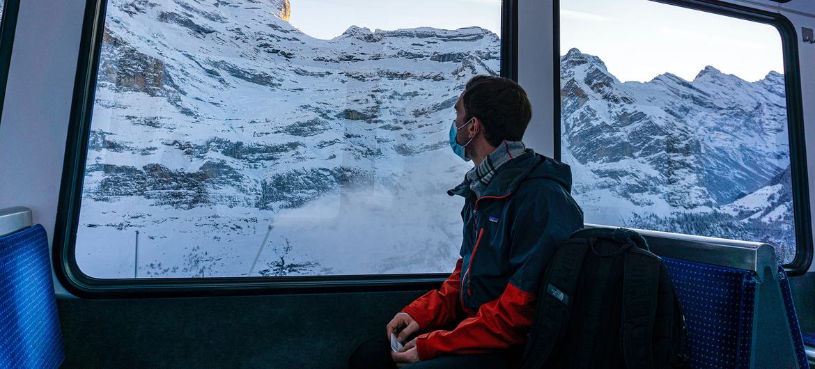 This young man traveling through the Swiss Alps by train during pandemic times dons a mask for Covid-19 protection. | Photograph courtesy of UN
