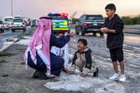 A man and children toss handfuls of hail particles picked up off the side of a road after a storm in the Umm al-Haiman district, about 55 kilometers south of Kuwait City, on 27 December 2022. (Photo by YASSER AL-ZAYYAT / AFP)