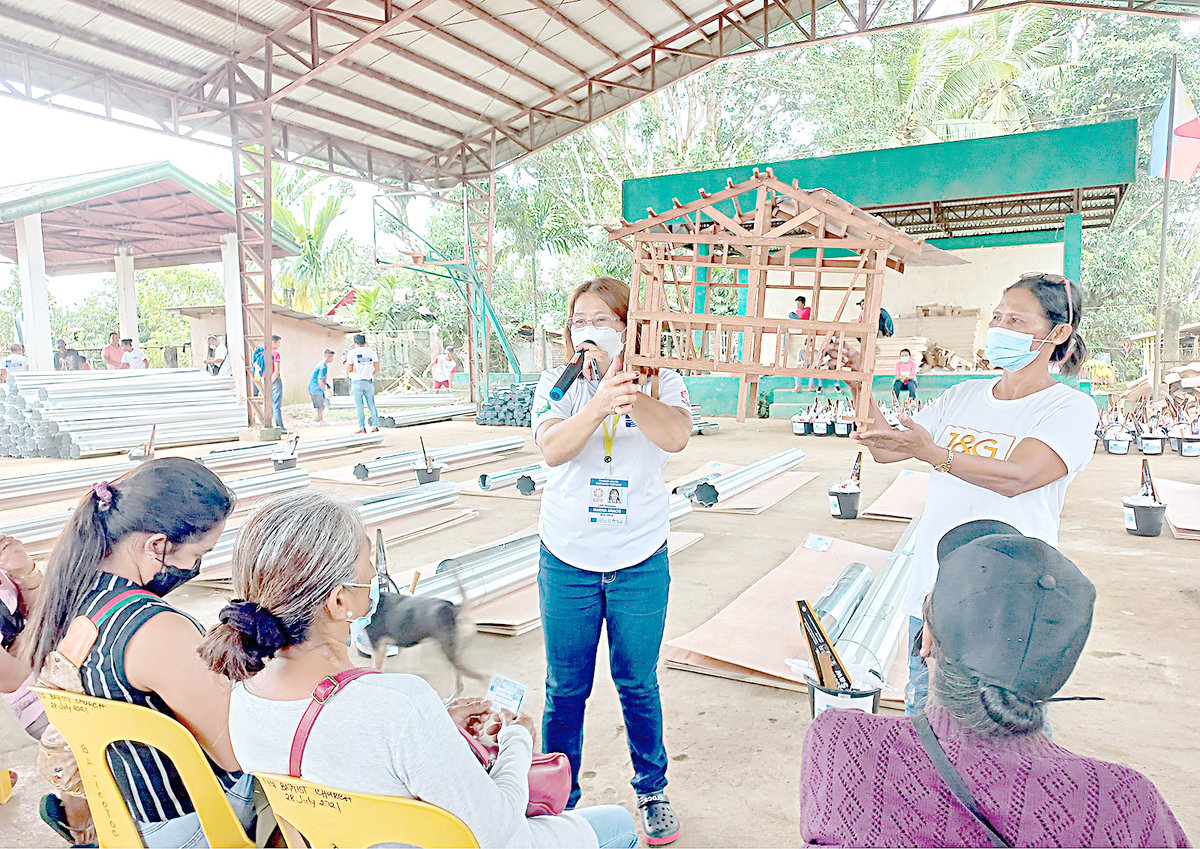 Heads of affected households listen as CARE staff show a prototype of a Build Back Better and Safer shelter in Barangay Balicotoc, Ilog, Negros Occidental.