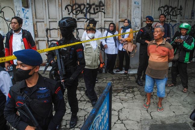 Bystanders look on as police secure the site of a suicide bombing outside a police station at Astanaanyar in Bandung, West Java province, on December 7, 2022. - A police officer was killed and several others were injured in a suicide bombing attack on a police station in Indonesia's West Java province on Tuesday, police said. (Photo by TIMUR MATAHARI / AFP)