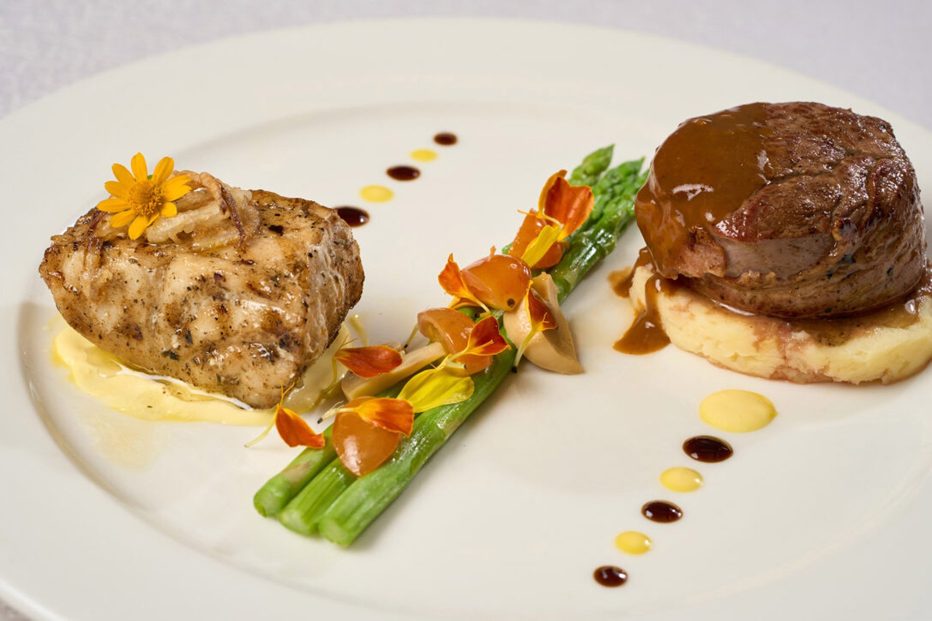 Filet Mignon and pan seared parrot fish drizzled with red wine reduction, safron sauce, mashed potato and asparagus spears.