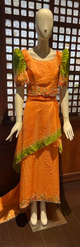 A tangerine terno made of polyester silk and contrasted by apple green, accentuated by machine-embroidered Santana flowers.