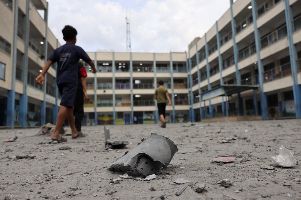 Palestinian children walk past debris in the courtyard of a school run by the United Nations Relief and Works Agency for Palestine refugees following Israeli airstrikes targeting Gaza City on 9 October 2023. The Israeli army said. (Photo by Mohammed ABED / AFP)