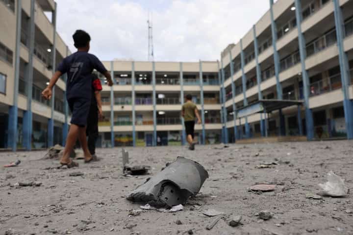 Palestinian children walk past debris in the courtyard of a school run by the United Nations Relief and Works Agency for Palestine refugees following Israeli airstrikes targeting Gaza City on 9 October 2023. The Israeli army said. (Photo by Mohammed ABED / AFP)