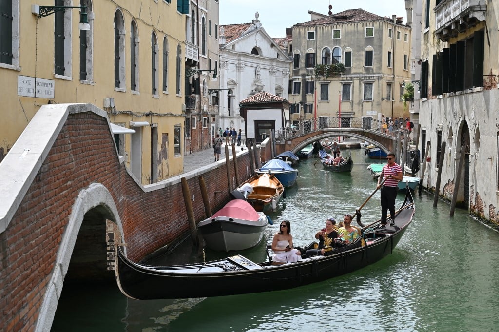 FILE PHOTO: A view taken on 31July 2023 shows tourists taking a Gondola ride across a canal in Venice. UNESCO is recommending that Venice be placed on the list of World Heritage in Danger, as "insufficient" measures have been taken to fight the deterioration of the site due in particular to mass tourism and climate change. (Photo by ANDREA PATTARO / AFP)