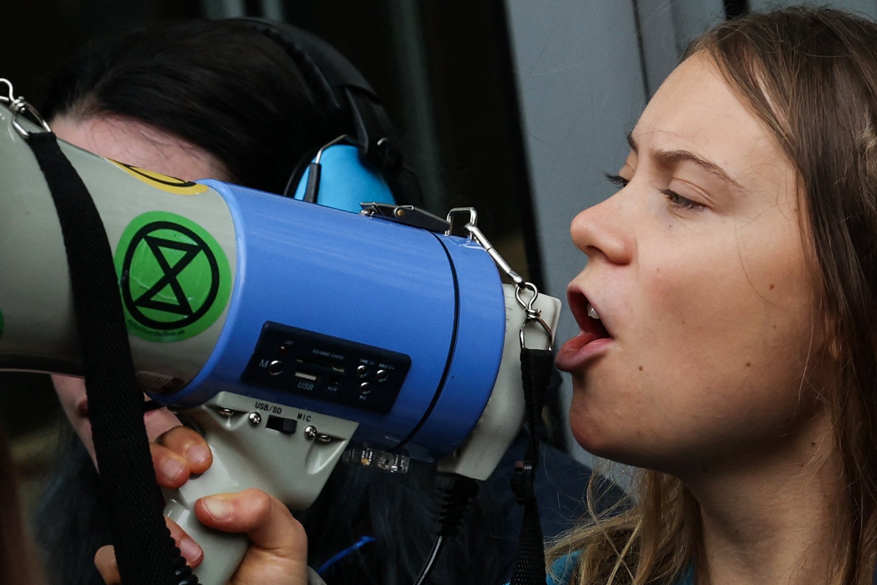 Swedish climate activist Greta Thunberg chants slogans in loud speaker as she sits in front of the entrance of the Bank JPMorgan in Canary Wharf, in London, on October 19, 2023 during a protest action against the company. Climate activists groups set a series of protests actions in the sidelines of the Energy Intelligence Forum taking place in London from October 17 to October 19. (Photo by Daniel LEAL / AFP)