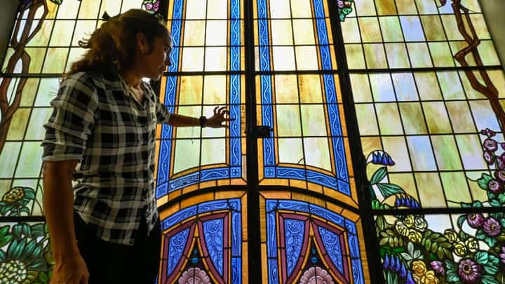 The teacher of stained glass restoration at the School Workshop of Havana, Mirell Vázquez, talks in front of a historical stained glass door on November 7, 2023, in Havana. The magic of the union of light and colorthe art of stained glasshas flourished over the centuries in Havana, where restoration work is helping to preserve this jewel of Cuban architecture. (Photo by ADALBERTO ROQUE / AFP)