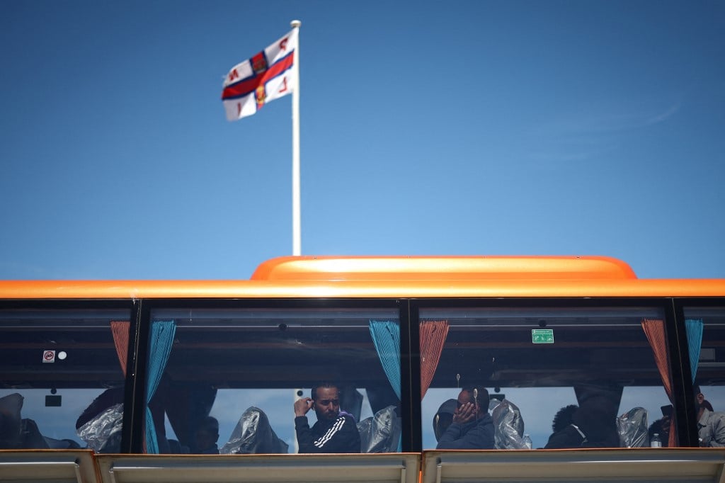 FILE PHOTO: Migrants look out from the window of a bus that will take them for processing, in Dungeness, on the southeast coast of England, on 16 August 2023 after being pick up at sea by a Royal National Lifeboat Institution (RNLI) lifeboat while crossing the English Channel from France. (Photo by HENRY NICHOLLS / AFP)