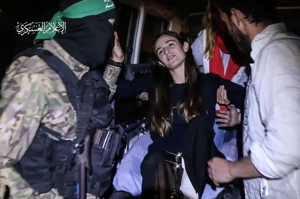 An image grab from a handout video released by the Hamas Media Office shows a Hamas fighter and Red Cross medics helping newly released Israeli hostage Maya Regev, 21, into a Red Cross vehicle, in the Gaza Strip early on 26 November 2023. Hamas on 25 November, released a second group of Israeli and foreign civilians it had been holding hostage in the Gaza Strip in exchange for Palestinian prisoners, after an hours-long unexpected delay set nerves on edge. Israeli authorities said 13 Israelis and four Thai citizens had returned to Israel. (Photo by HAMAS MEDIA OFFICE / AFP)
