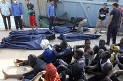 FILE PHOTO: African migrants rescued from a ship off the coast of Zuwara, about 130 kilometres west of the Libyan capital Tripoli, sit alongside of bodies of others who died, at the dock in the capital's naval base on 18 June 2018. (Photo by MAHMUD TURKIA / AFP)