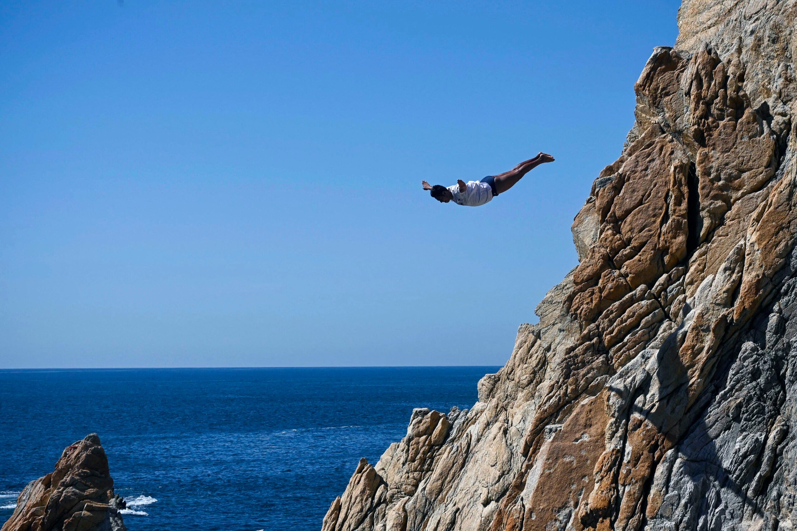 A cliff diver of La Quebrada performs after resuming activities following the passage of Hurricane Otis in Acapulco, Guerrero state, Mexico on 8 December 2023. (Photo by Francisco Robles / AFP)