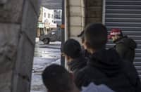Palestinian youths observe an Israeli army patrol car from the safety of a corner at the entrance of the Jenin refugee camp in the occupied West Bank on December 13, 2023, as battles continue between Israel and the militant movement Hamas in Gaza. Photo by MARCO LONGARI / AFP