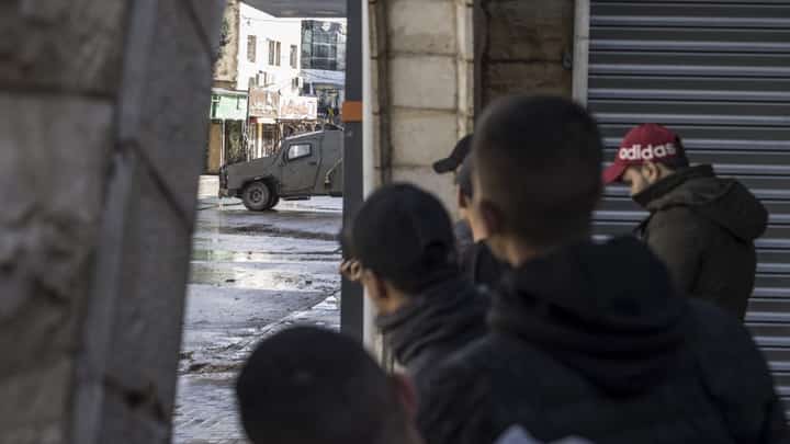 Palestinian youths observe an Israeli army patrol car from the safety of a corner at the entrance of the Jenin refugee camp in the occupied West Bank on December 13, 2023, as battles continue between Israel and the militant movement Hamas in Gaza. Photo by MARCO LONGARI / AFP