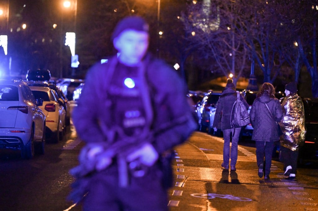 People being caught up in a shooting incident walks past an armed police man near the Charles University in central Prague, on December 21, 2023. Photo by Michal CIZEK / AFP
