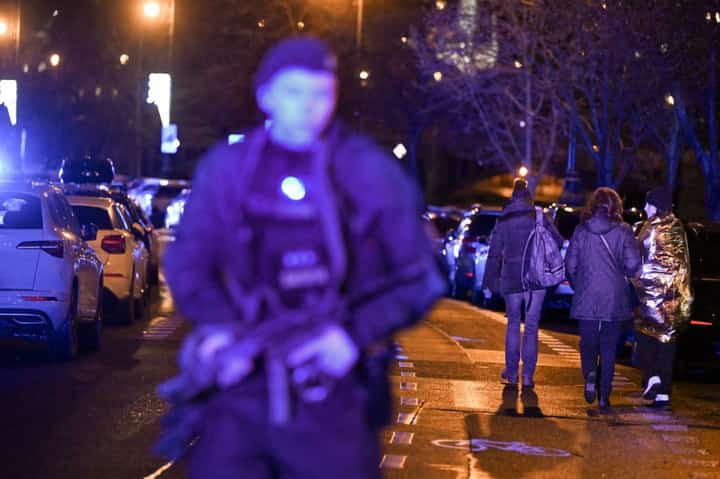 People being caught up in a shooting incident walks past an armed police man near the Charles University in central Prague, on December 21, 2023. Photo by Michal CIZEK / AFP