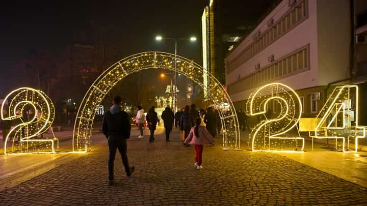 Pedestrians walk through a 2024 illuminated sign displayed in downtown Pristina on 30 December 2023, ahead of the New Year celebrations in Kosovo. (Photo by Armend NIMANI / AFP)