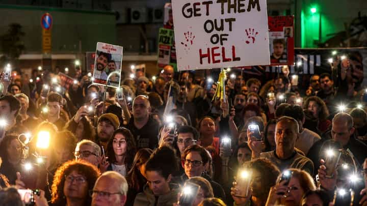 Relatives and supporters light their phones around a placard reading "Get them out of hell" during a rally calling for the release of Israeli hostages held in Gaza since the 7 October attacks by Hamas in southern Israel, in Tel Aviv on 30 December 2023. (Photo by AHMAD GHARABLI / AFP)