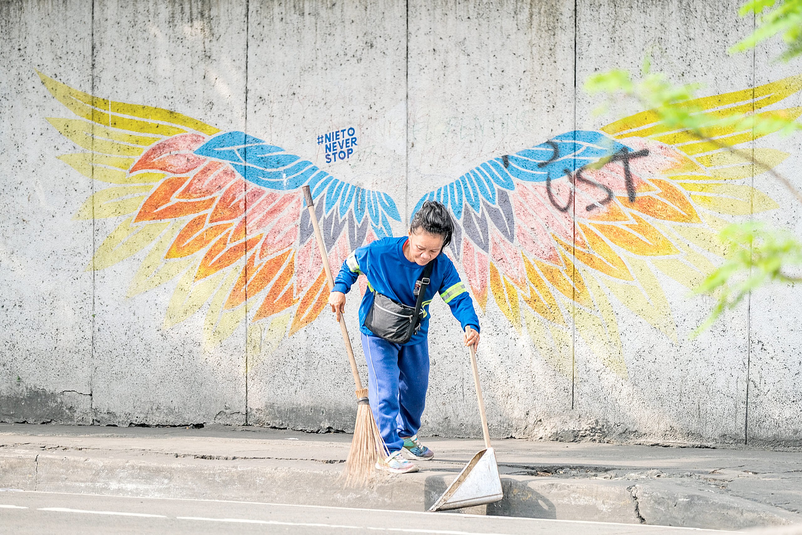 A woman in work clothes sweeps the street with a broom and dustpan along Legarda Street in Manila on 6 December