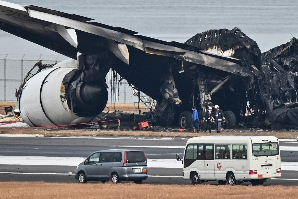 Officials look at the burnt wreckage of a Japan Airlines (JAL) passenger plane on the tarmac at Tokyo International Airport at Haneda in Tokyo on 3 January 2024, the morning after the JAL airliner hit a smaller coast guard plane on the ground. Five people aboard a Japan coast guard aircraft died on 2 January when it hit a Japan Airlines passenger plane on the ground in a fiery collision at Tokyo's Haneda airport. (Photo by Richard A. Brooks / AFP)