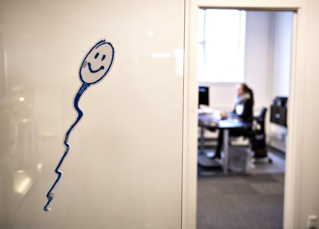 A drawing of a smiling sperm is seen on a wall at a fertility center, while a woman works at her desk in the background.