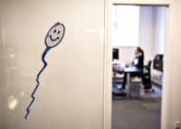 A drawing of a smiling sperm is seen on a wall at a fertility center, while a woman works at her desk in the background.