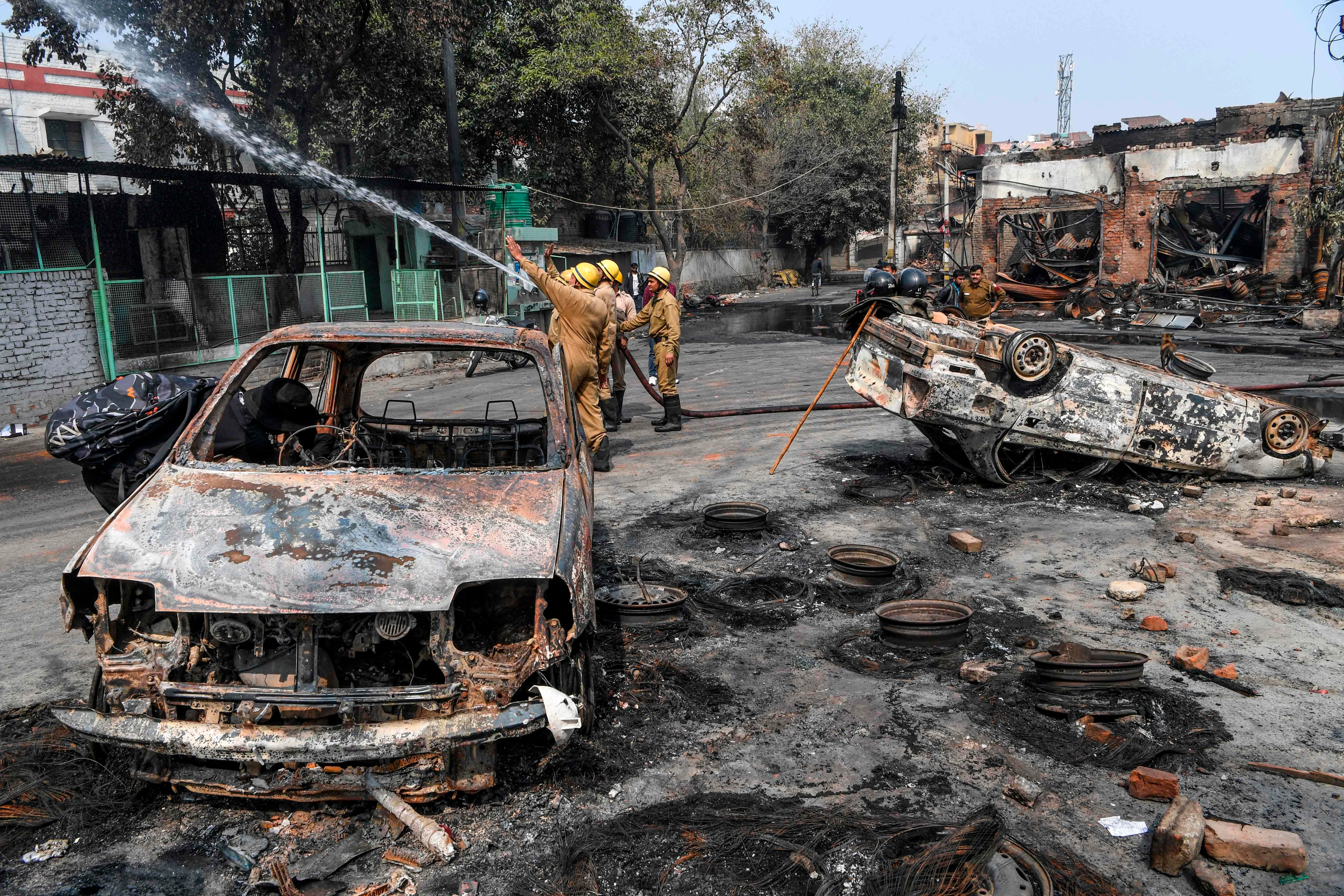 Firefighters hold a water pipe to douse burnt-out tyre market premises following clashes between people supporting and opposing a contentious amendment to India's citizenship law, in New Delhi on February 26, 2020.