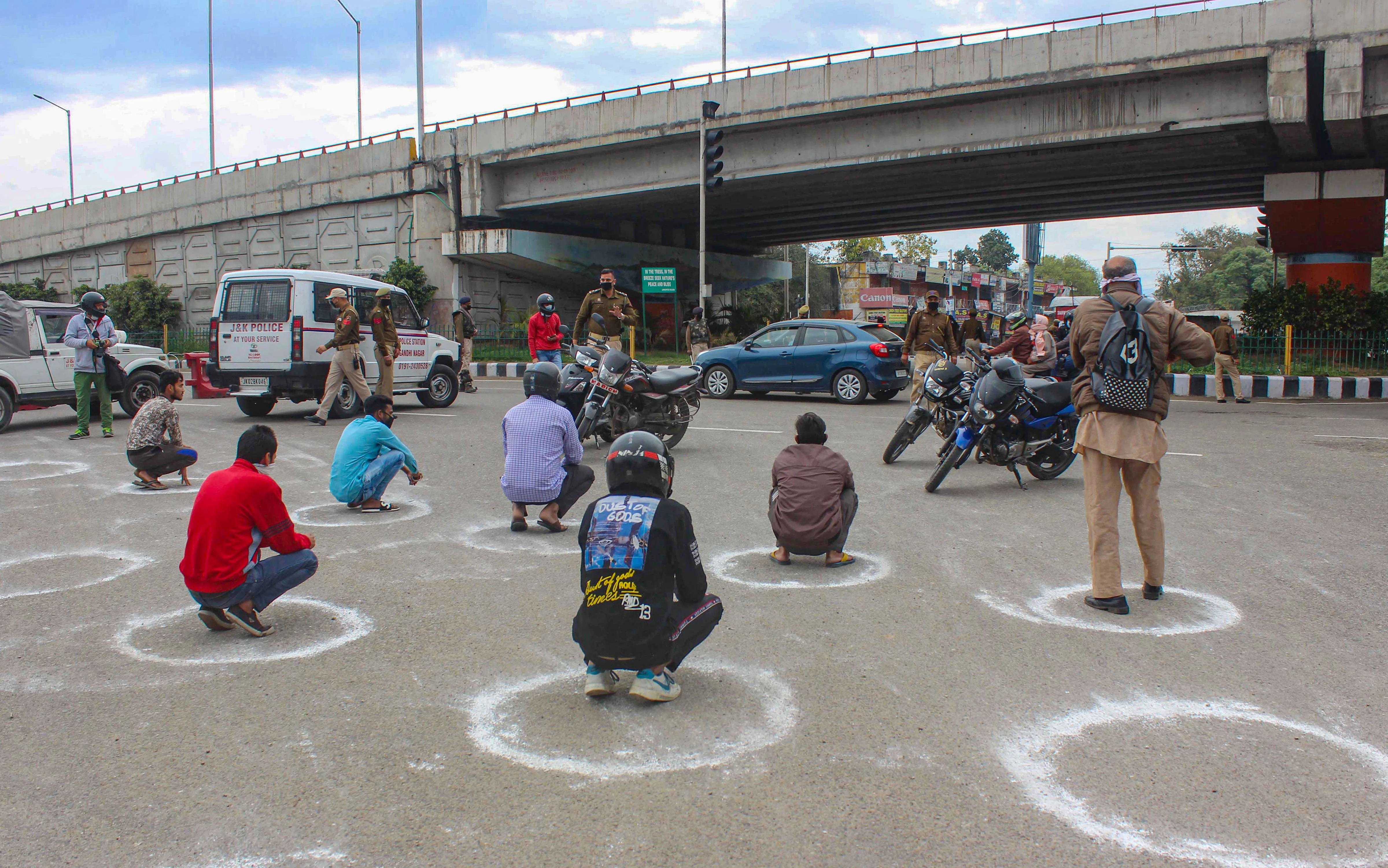 Policemen punish offenders, seated in marked circles to maintain social distancing, who violated the lockdown guidelines by venturing out of their homes unnecessarily during the 21-day complete lockdown to contain the spread of the novel coronavirus, at Vikram Chowk in Jammu, Wednesday, March 25, 2020.
