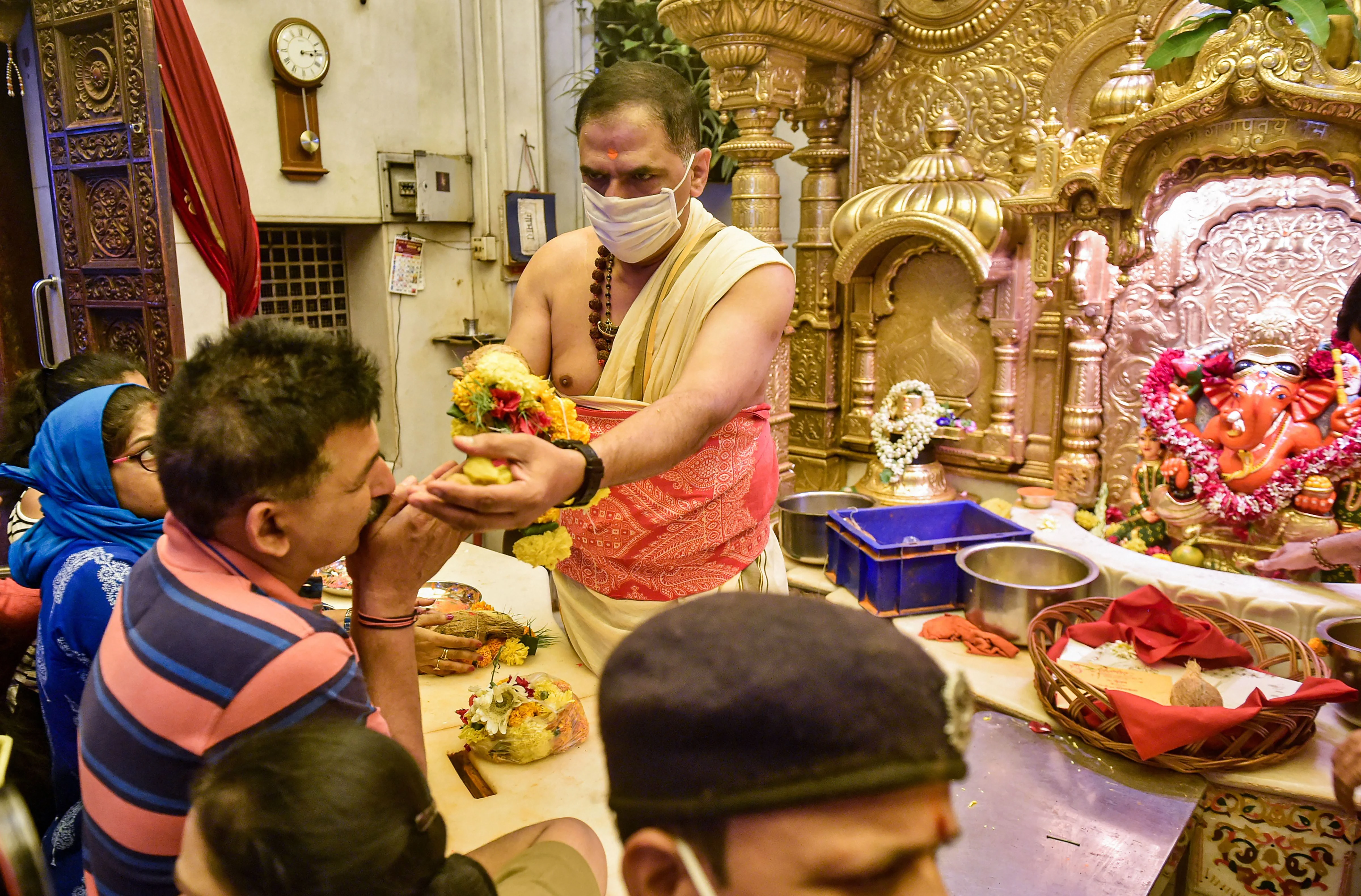 priest wearing protective masks as a precautionary measure against the novel coronavirus (COVID-19), offers 'prasad' to a devotee at Siddhivinayak Temple in Mumbai