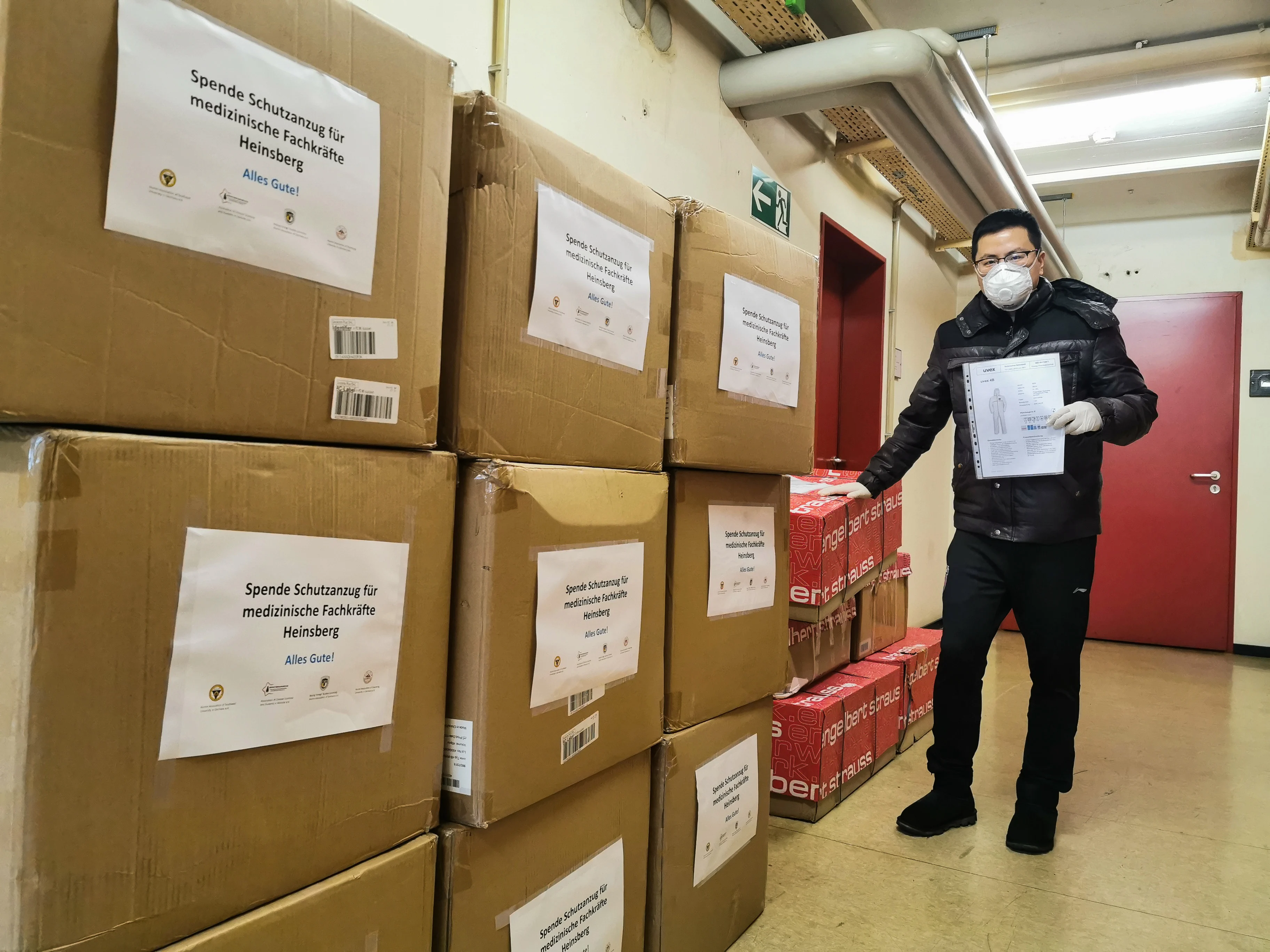 A volunteer stands next to packages containing protective suits in Heinsberg, Germany, on March 6, 2020. A group of overseas Chinese living in Frankfurt, Germany have sent some 900 protective suits, packed in 25 boxes, to Heinsberg, a German region heavily hit by COVID-19.