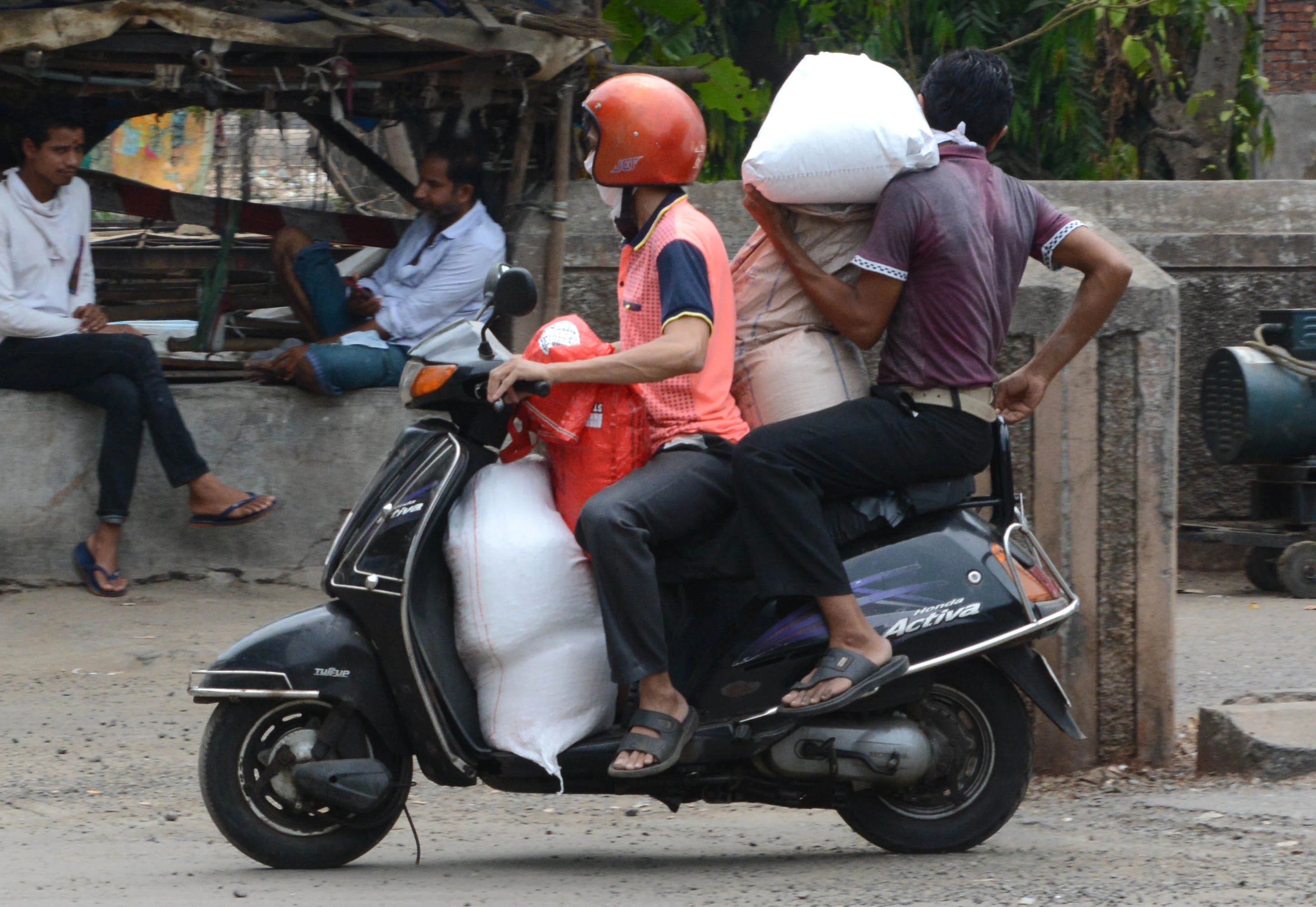 People carrying sacks filled with essential things on two-wheeler.