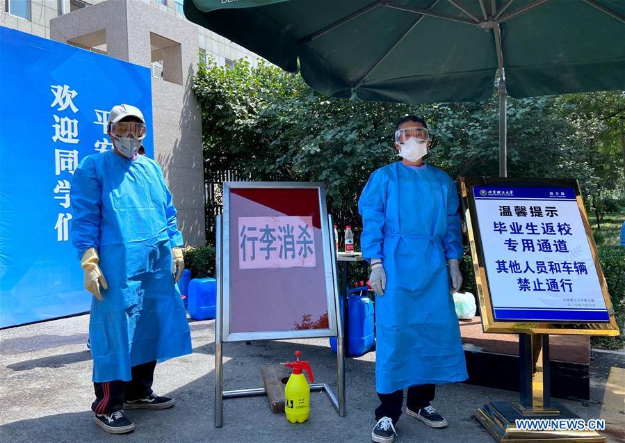 Two staff members prepare to disinfect students' luggage at the gate of Beijing Institute of Technology in Beijing, capital of China, June 6, 2020.