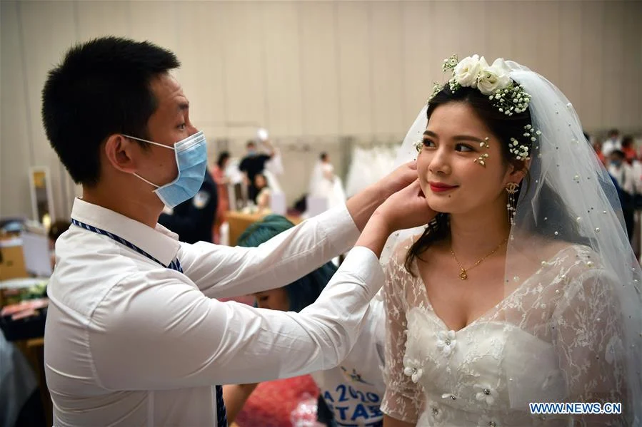 Chen Jianming, a senior nurse from Hunan Provincial People's Hospital who once was dispatched to Huanggang City in Hubei Province for the fight against COVID-19, helps his wife Tang Chan, who is also a medical worker, wear earrings at a resort in Sanya City, south China's Hainan Province, June 6, 2020. A group wedding ceremony was held here Saturday for newly-married couples from 15 provinces nationwide who once worked to fight against the COVID-19 outbreak.